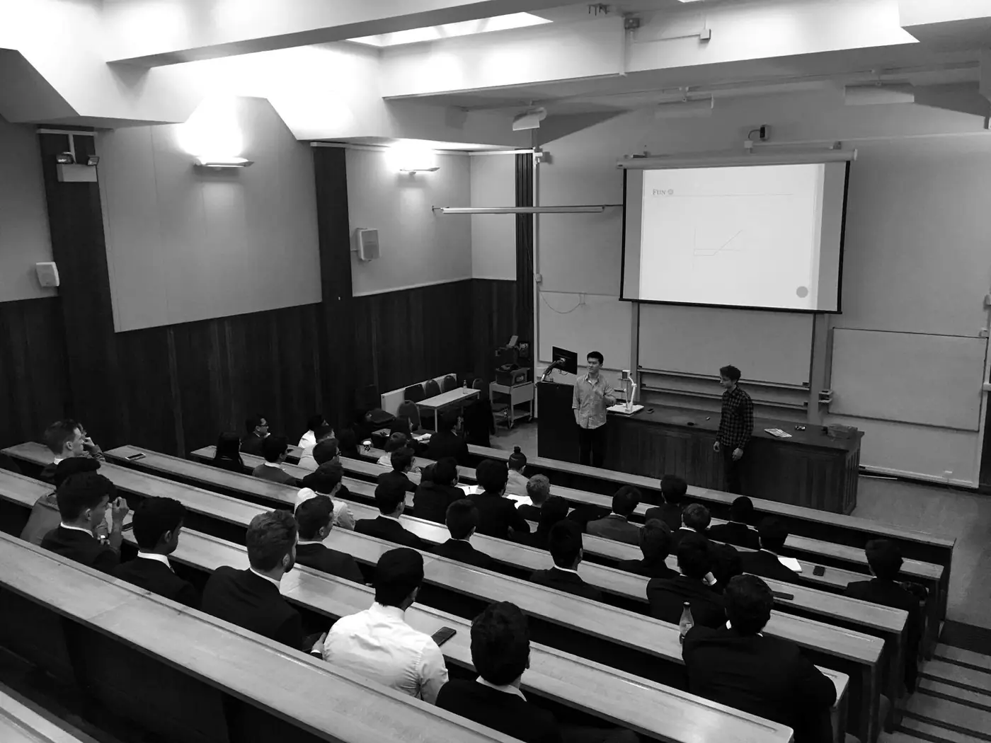 Black and white photo of a stock pitch in a tiered lecture theatre